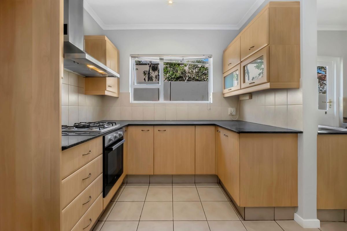 A functional U-shaped kitchen featuring light wood cabinetry, dark countertops, tiled splashbacks, and built-in stainless steel oven and extractor fan.