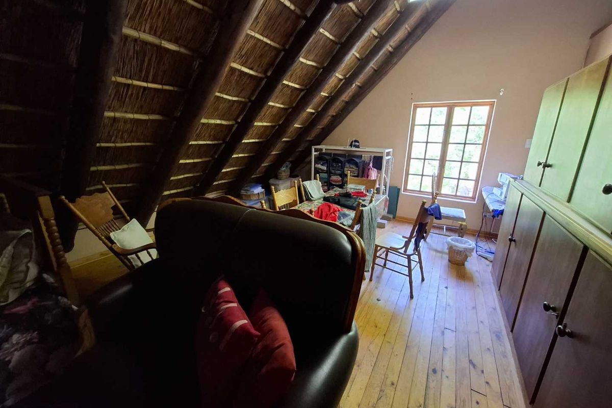 Attic-style living space featuring exposed thatched roof rafters, timber flooring, and built-in wooden cabinetry under a pitched ceiling.