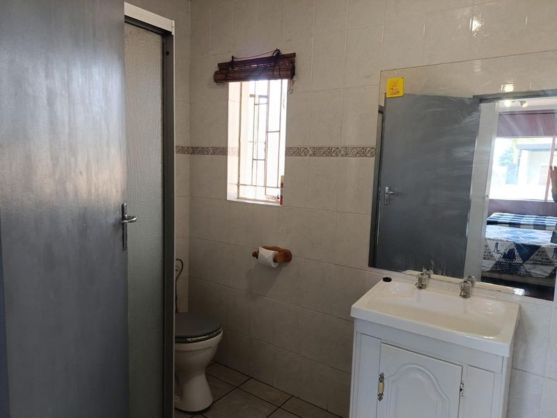 A functional bathroom featuring a vanity cabinet with basin, a toilet, and a shower enclosure with tiled walls and flooring.