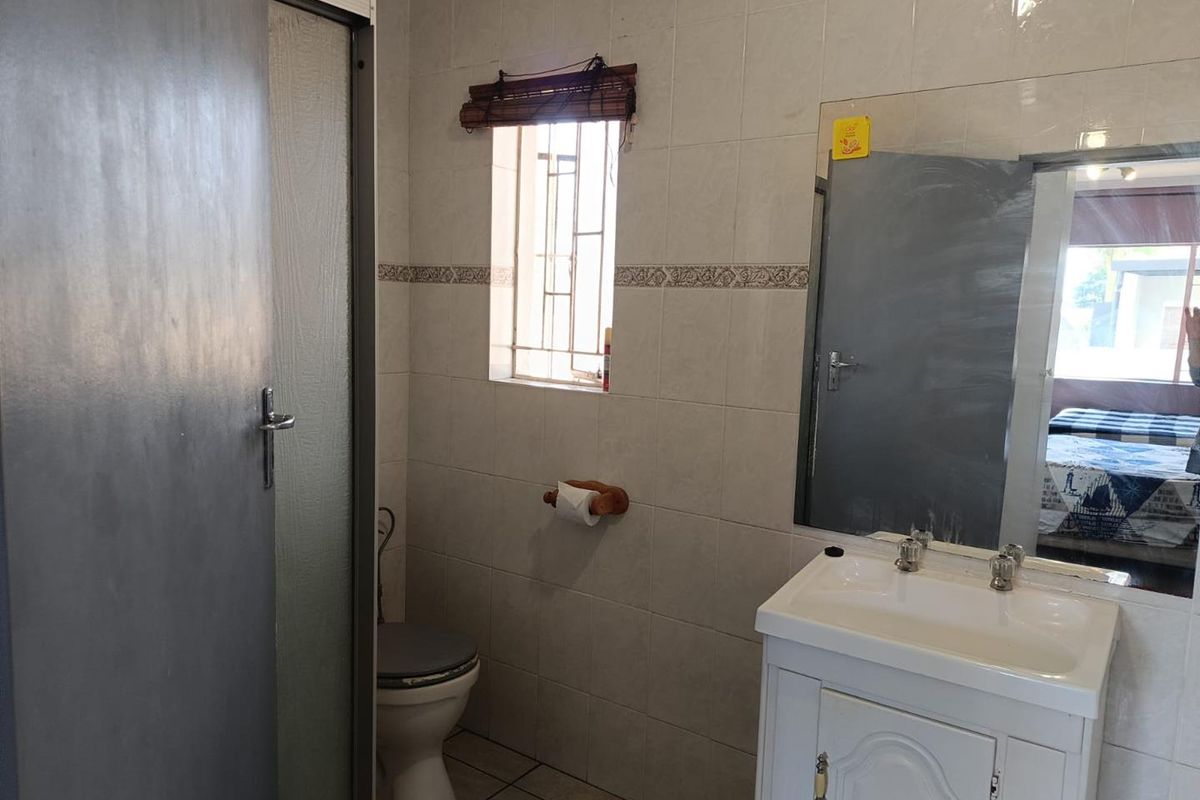A functional bathroom featuring a vanity cabinet with basin, a toilet, and a shower enclosure with tiled walls and flooring.