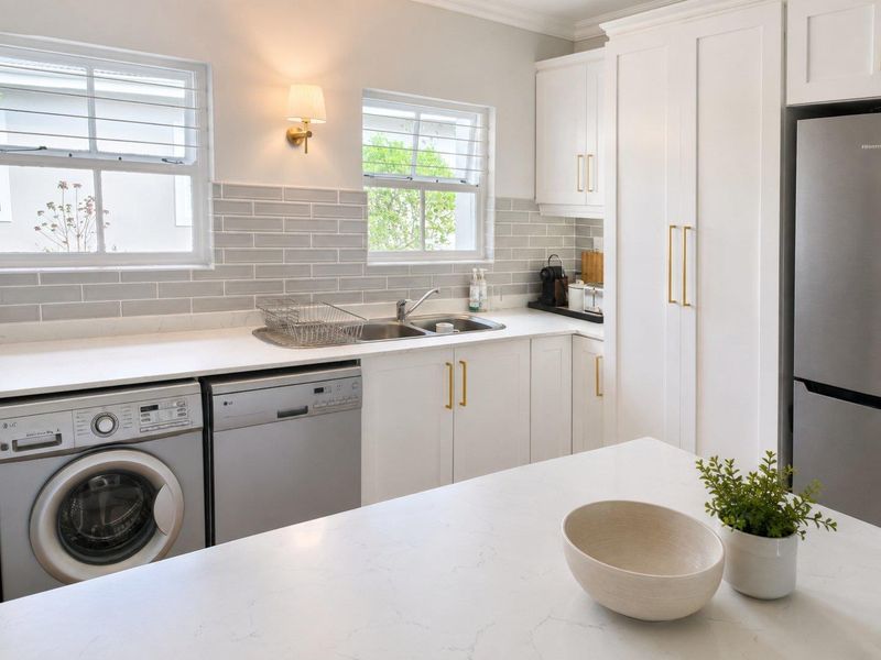 Modern kitchen featuring white shaker cabinetry, quartz countertops, subway tile backsplash, and integrated laundry appliances with elegant brass hardware finishes.