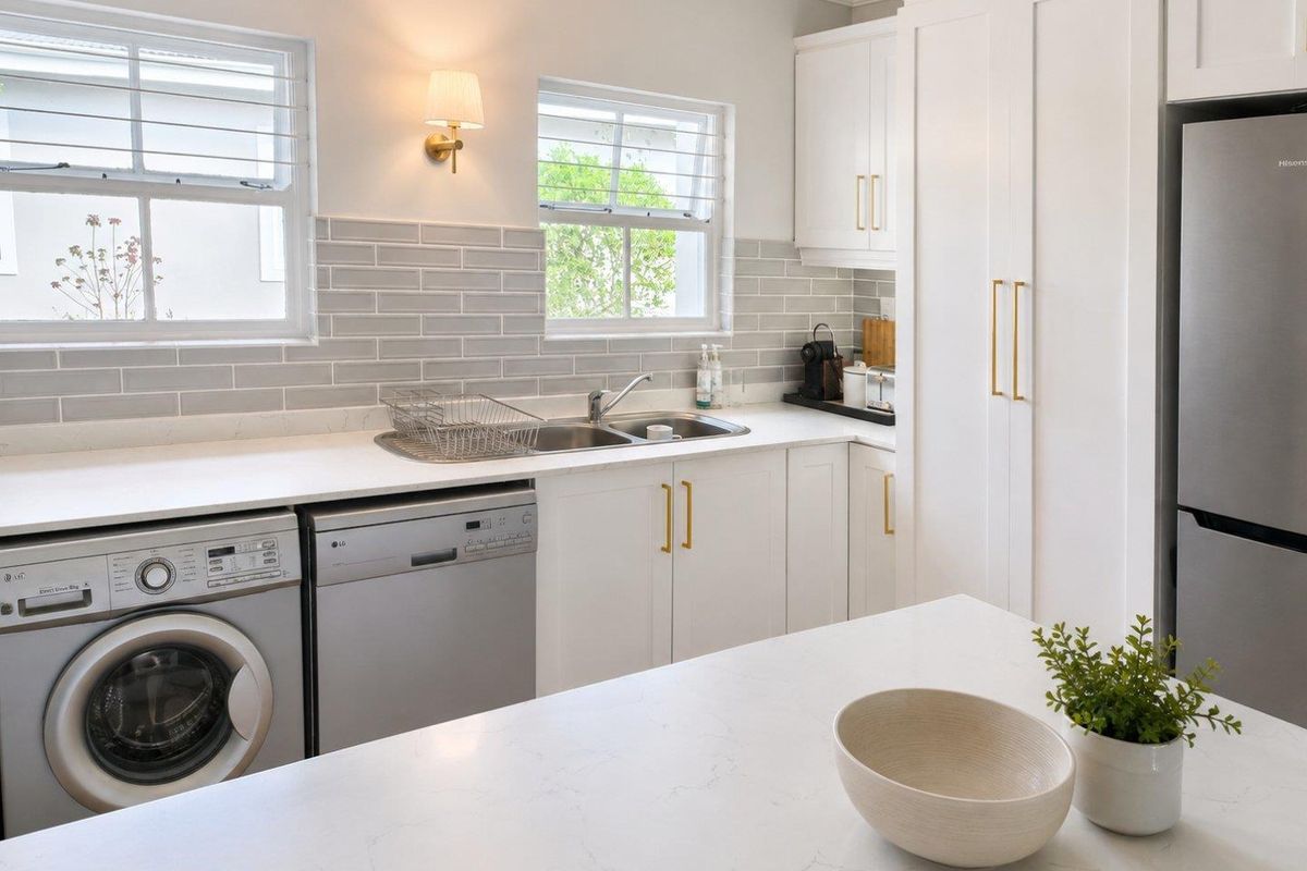 Modern kitchen featuring white shaker cabinetry, quartz countertops, subway tile backsplash, and integrated laundry appliances with elegant brass hardware finishes.