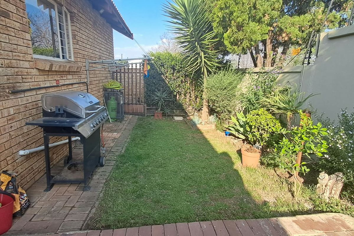 A private rear garden featuring a paved patio area, a small lawn, and secure boundary walls with perimeter security.