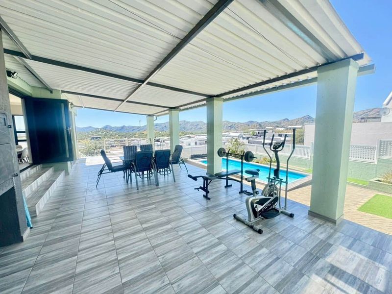 Spacious covered patio featuring tiled flooring, overlooking a swimming pool and scenic mountain views, ideal for outdoor entertaining and relaxation.