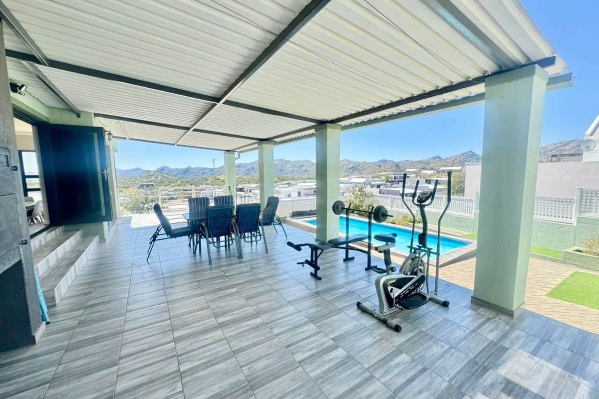 Spacious covered patio featuring tiled flooring, overlooking a swimming pool and scenic mountain views, ideal for outdoor entertaining and relaxation.
