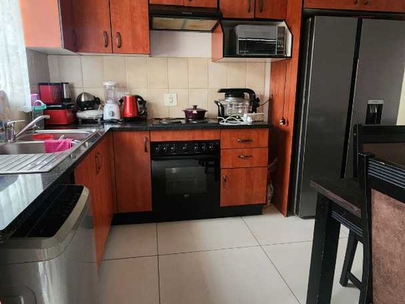 A functional kitchen featuring wood-finish cabinetry, dark countertops, integrated oven and hob, and tiled flooring, providing a practical workspace for daily cooking.