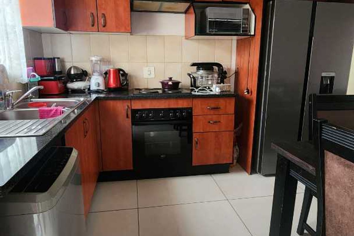 A functional kitchen featuring wood-finish cabinetry, dark countertops, integrated oven and hob, and tiled flooring, providing a practical workspace for daily cooking.