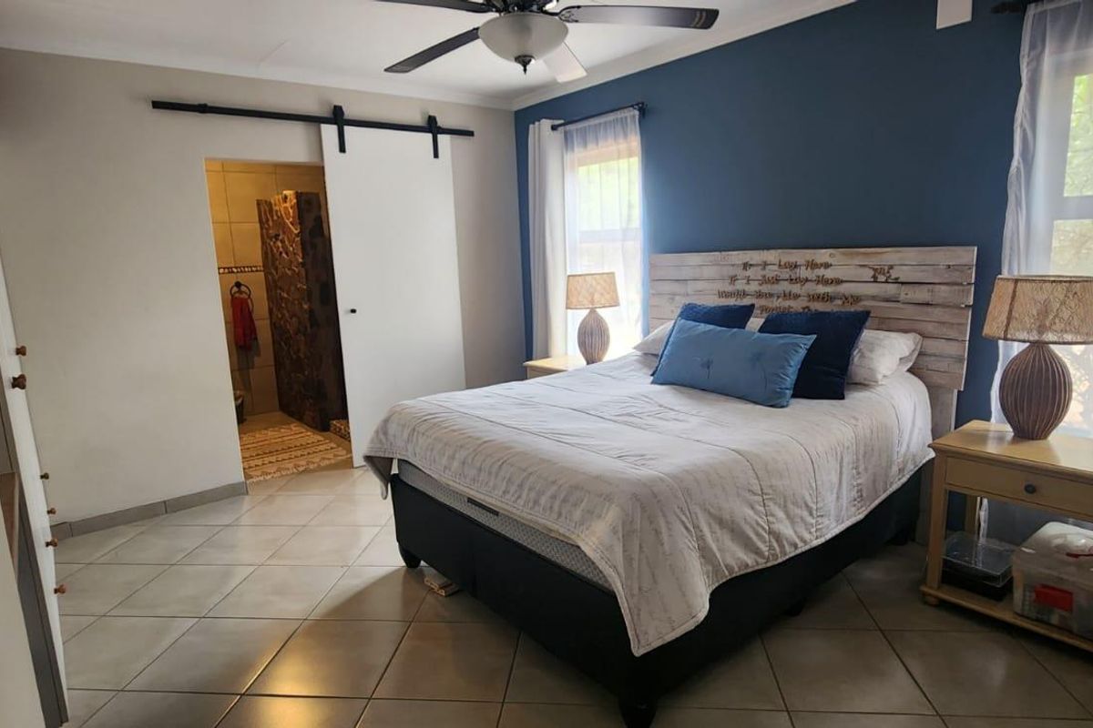 A bedroom featuring tiled flooring, a ceiling fan, and a sliding barn door providing access to an en-suite bathroom.