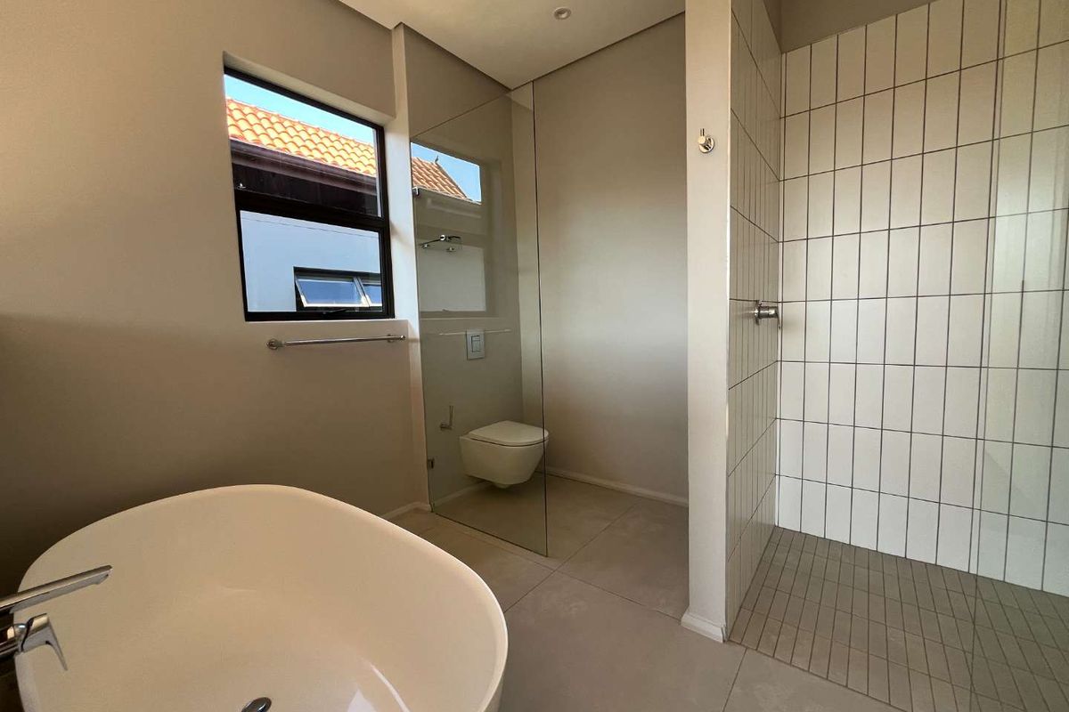 Modern bathroom featuring a sleek freestanding bathtub, a spacious walk-in shower with glass enclosure, and a wall-mounted toilet with neutral tiling.