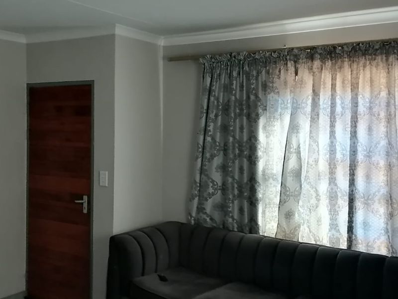 A living room featuring neutral wall paint, cove cornicing, a timber door, and a window with a curtain rod.