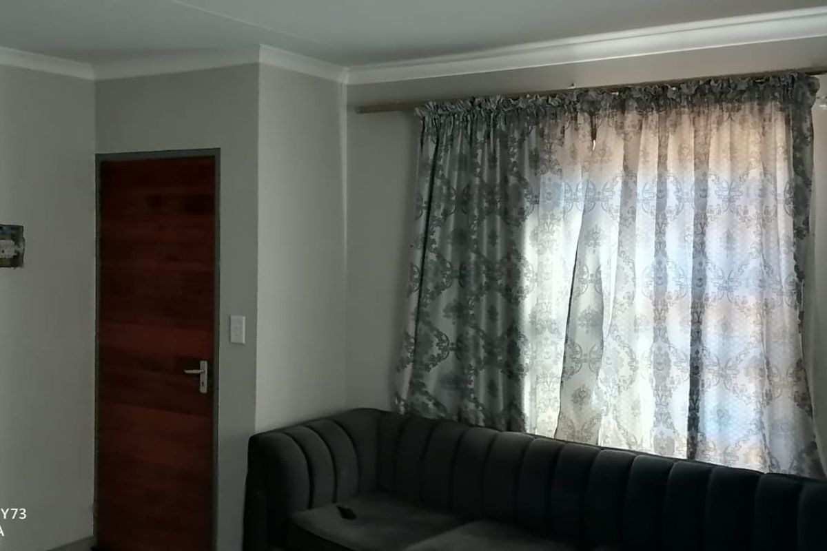 A living room featuring neutral wall paint, cove cornicing, a timber door, and a window with a curtain rod.