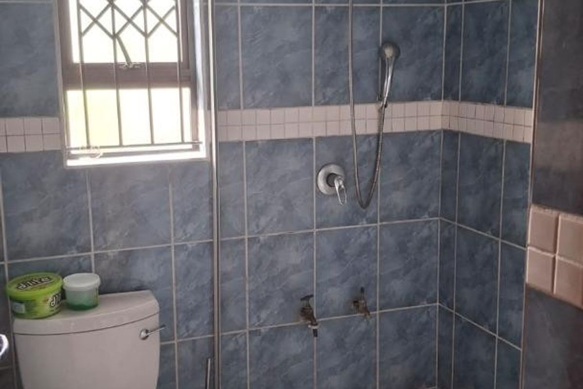 A functional bathroom featuring a tiled shower area, toilet, and security-fitted window, requiring cosmetic updates to modernize the dated finishes.