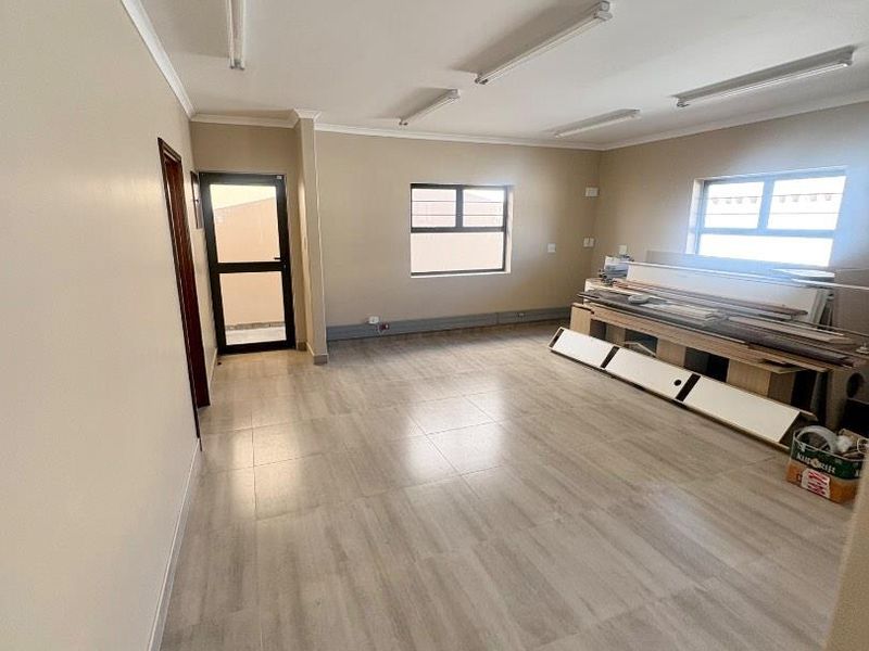 A spacious, empty office area featuring neutral walls, tiled flooring, and multiple fluorescent light fixtures, suitable for a professional workspace.