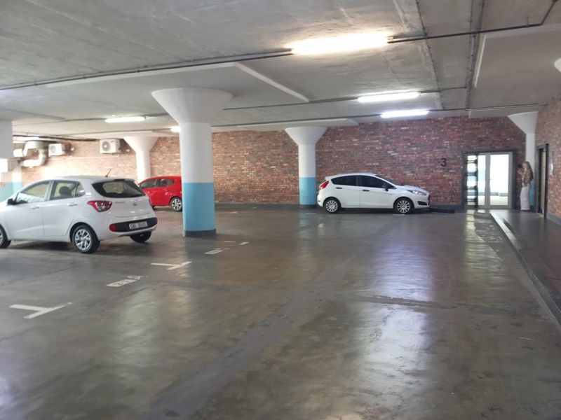 A covered parking garage featuring exposed brick walls, concrete columns, and marked parking bays with overhead fluorescent lighting.