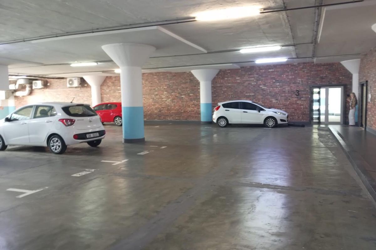 A covered parking garage featuring exposed brick walls, concrete columns, and marked parking bays with overhead fluorescent lighting.
