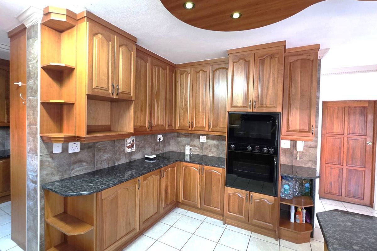 A traditional kitchen featuring warm-toned wooden cabinetry, dark granite countertops, built-in oven, and tiled flooring with a decorative recessed ceiling feature.