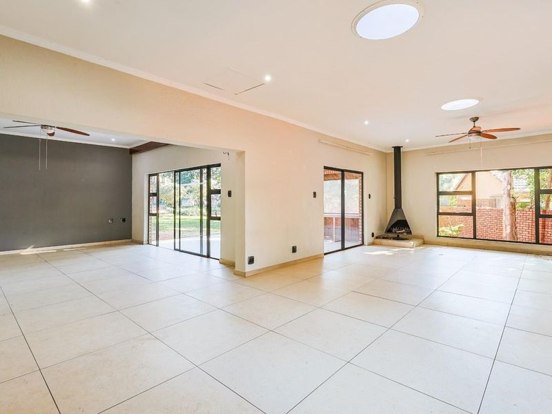 Spacious open-plan living area featuring large format floor tiles, a modern freestanding fireplace, multiple skylights, and sliding doors providing access to the outdoor space.