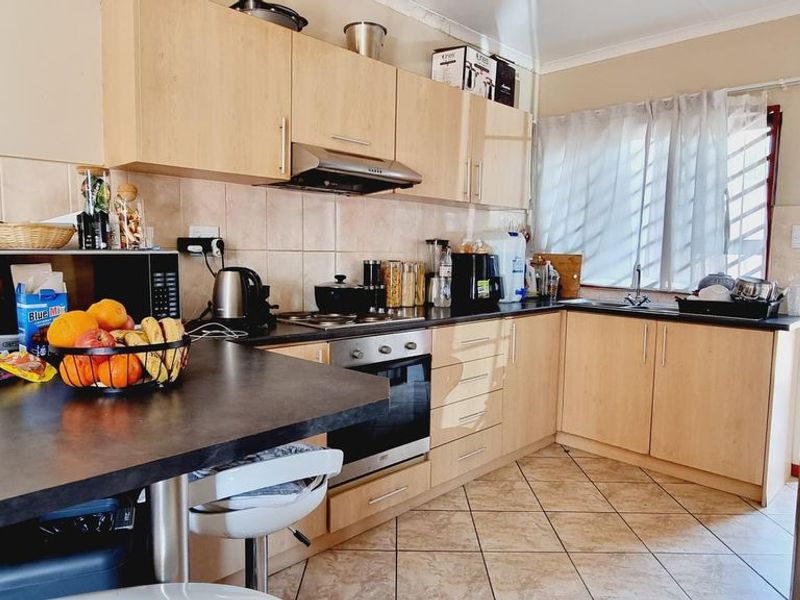 Functional kitchen featuring light wood-tone cabinetry, dark laminate countertops, built-in oven with extractor fan, and tiled flooring.