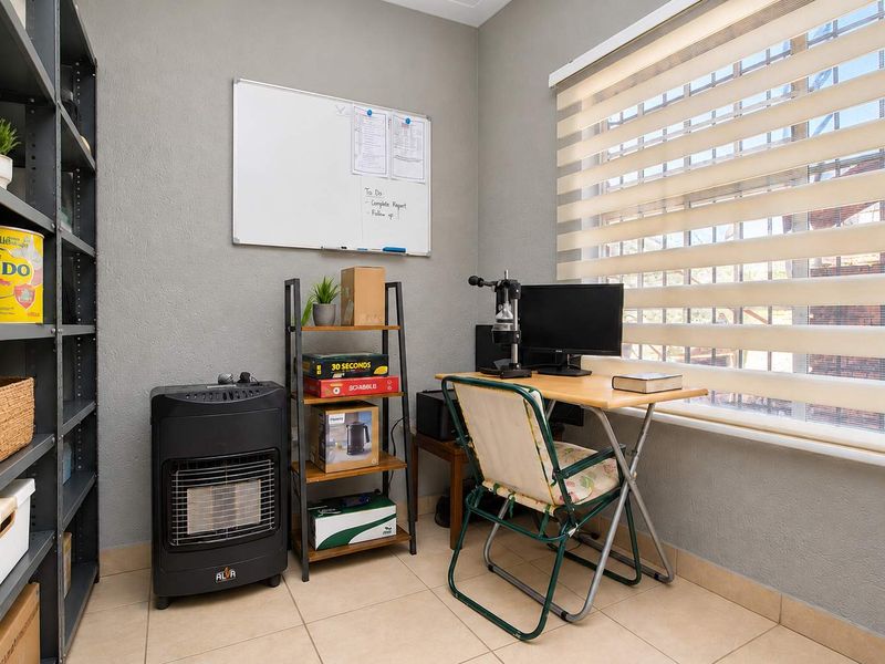 A functional home office space featuring neutral wall tones, tiled flooring, and adjustable roller blinds for natural light control.