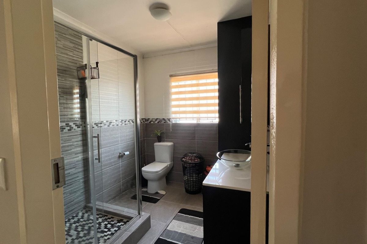 A modern bathroom featuring a glass-enclosed shower, tiled walls, a vanity with a vessel sink, and a toilet.