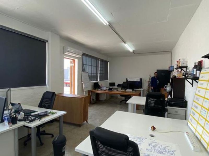 A functional office space featuring industrial-style windows, roller blinds, concrete flooring, and an integrated air conditioning unit.