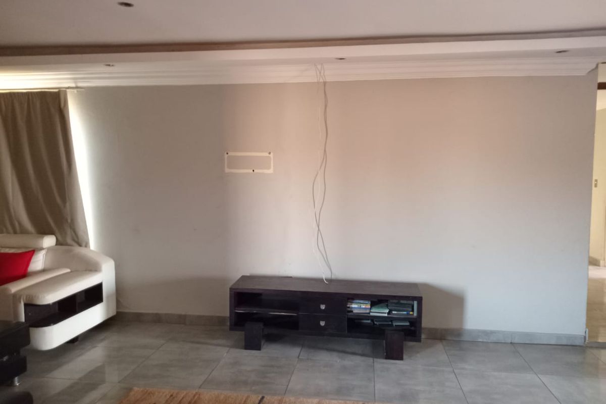 A living room featuring tiled flooring, recessed ceiling lighting, and a dedicated wall space for media equipment with exposed cabling.