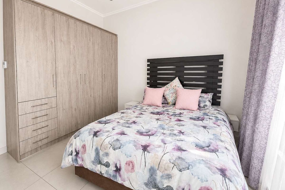 A well-maintained bedroom featuring neutral tiled flooring, recessed downlighting, and a large, modern built-in wardrobe with ample storage space.
