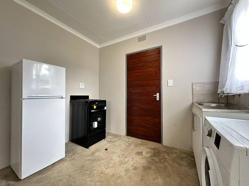A functional kitchen space featuring a stainless steel sink, built-in cabinetry, and a freestanding stove, with neutral walls and a solid timber door.