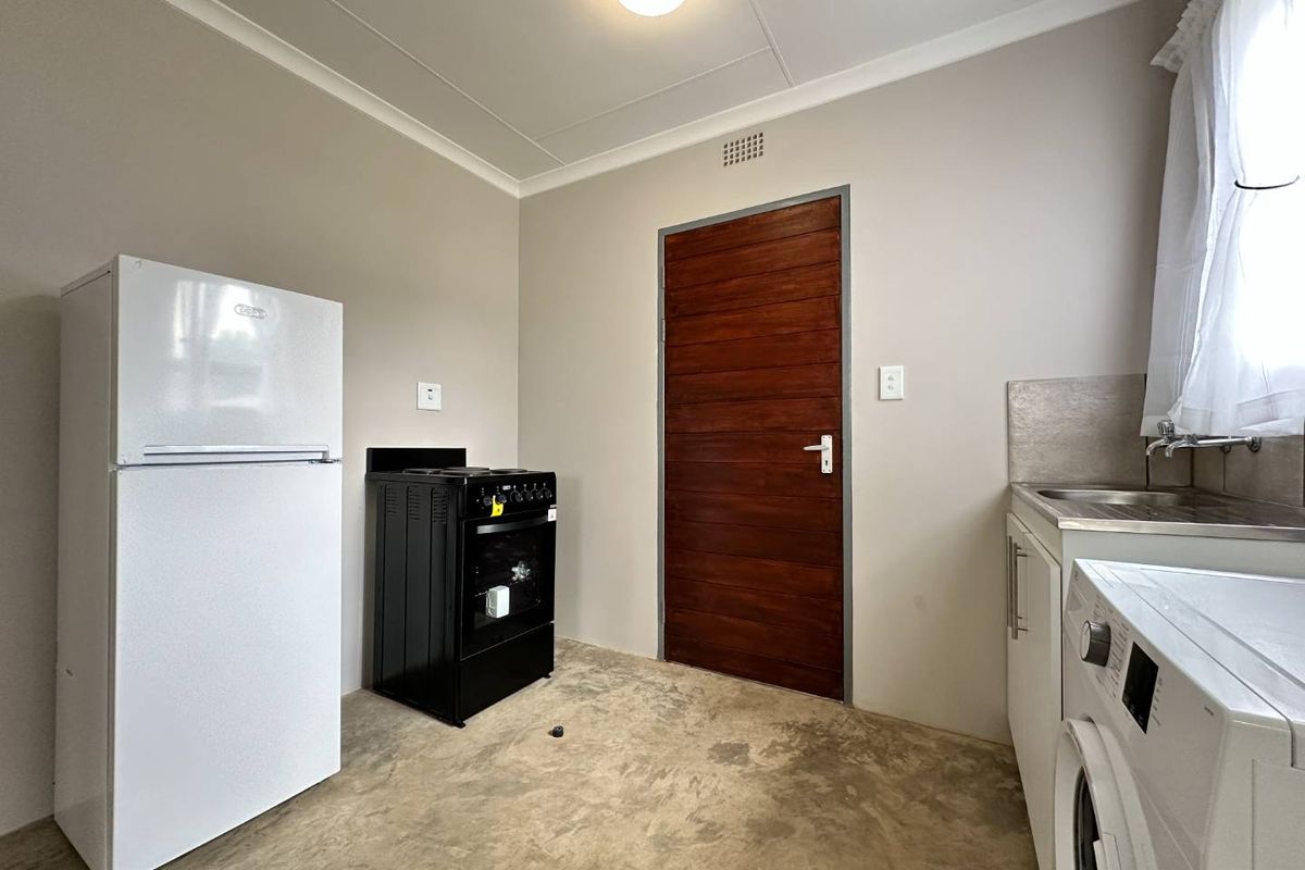 A functional kitchen space featuring a stainless steel sink, built-in cabinetry, and a freestanding stove, with neutral walls and a solid timber door.