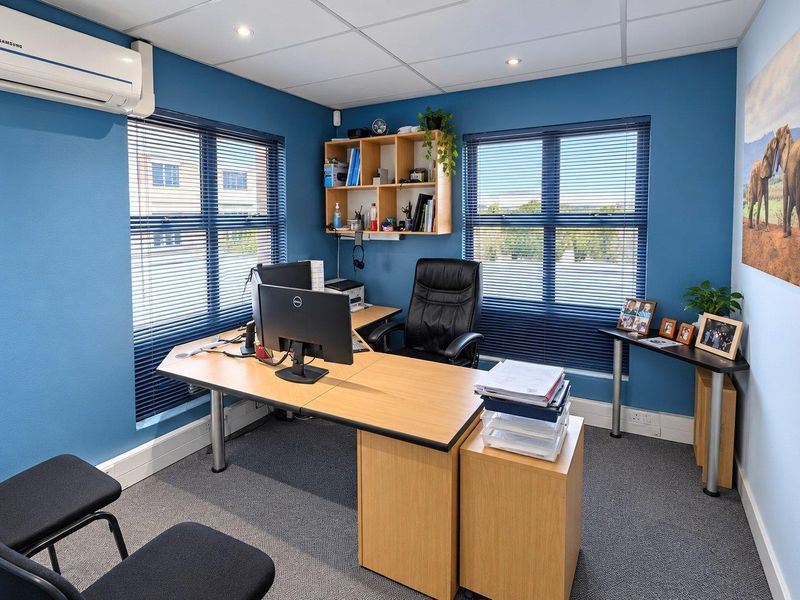 A well-maintained office space featuring blue walls, carpet flooring, a suspended ceiling with recessed lighting, and a wall-mounted air conditioning unit.