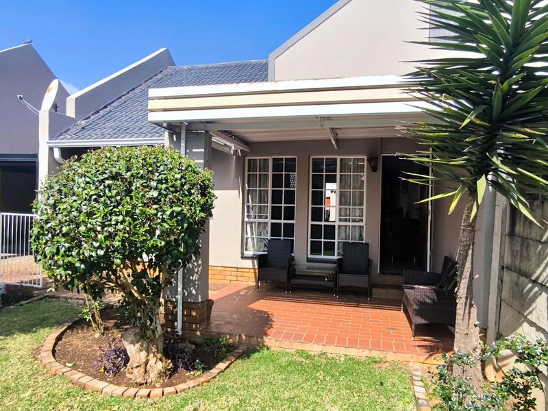 A well-maintained rear exterior view of the townhouse featuring a covered patio, brick paving, and a neat garden area.