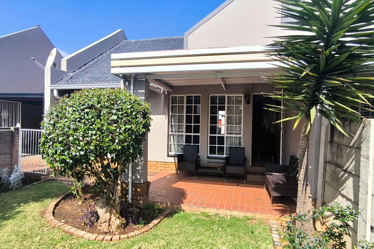 A well-maintained rear exterior view of the townhouse featuring a covered patio, brick paving, and a neat garden area.