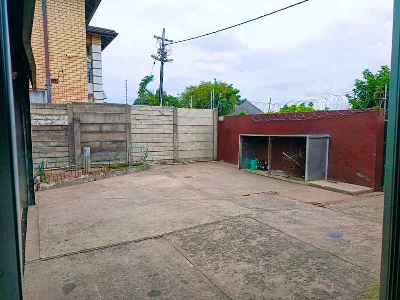 A paved rear courtyard area featuring a precast concrete boundary wall with security razor wire and a built-in storage structure.