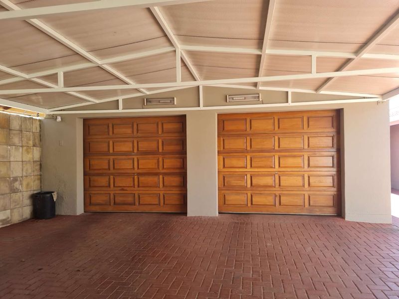 A well-maintained double garage featuring wooden doors, a covered carport area, and paved driveway, providing secure off-street parking.