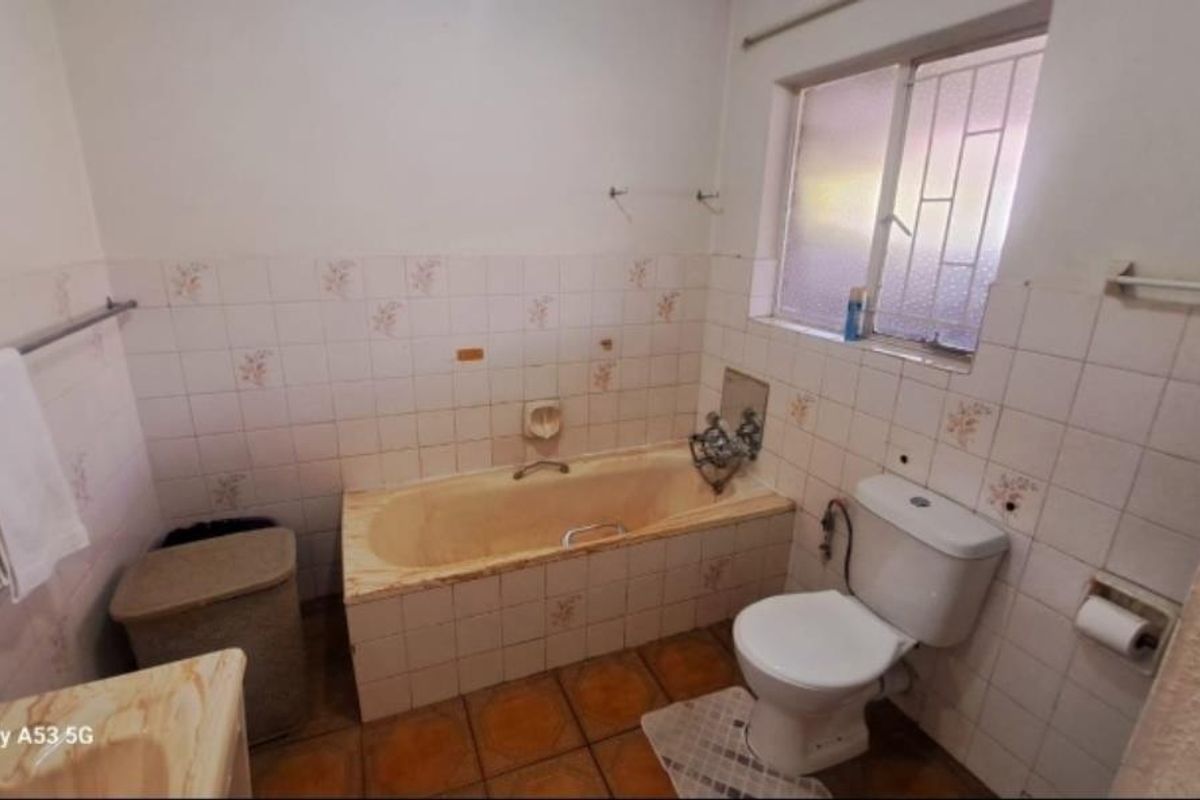 A dated bathroom featuring a built-in bathtub, standard toilet, and tiled walls with a window providing natural light.