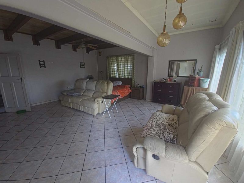 Spacious open-plan living area featuring tiled flooring, exposed timber ceiling beams, and pendant lighting, offering a versatile layout for various living arrangements.