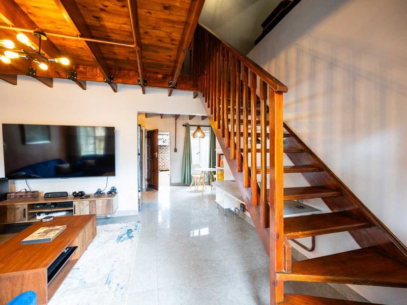 Open-plan living area featuring exposed timber ceiling beams, a wooden staircase with balustrade, and polished tiled flooring leading to an adjacent dining space.
