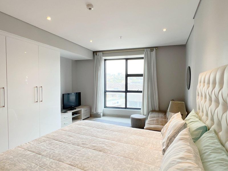 A well-maintained bedroom featuring a large window, recessed downlighting, and ample built-in wardrobe storage.