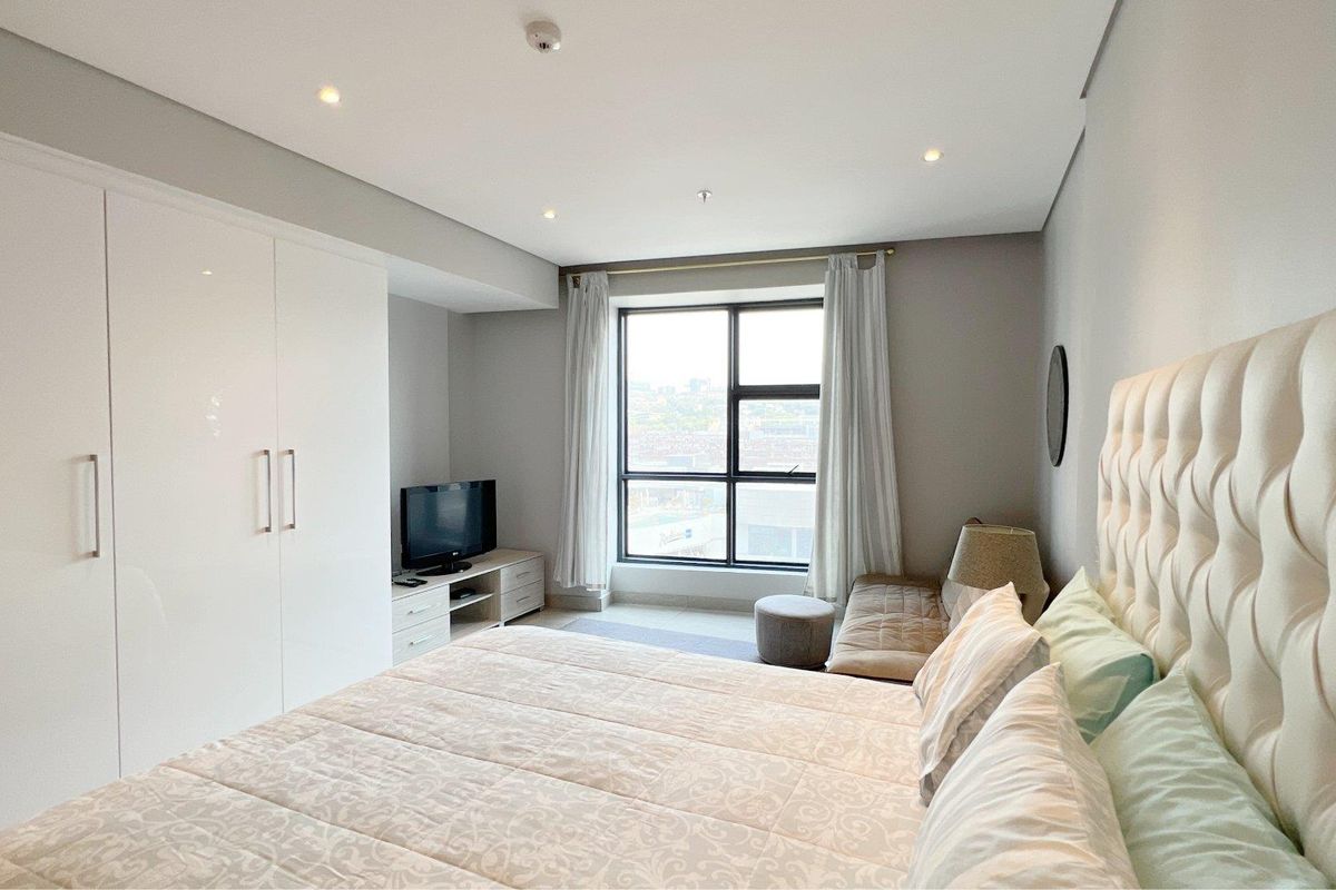A well-maintained bedroom featuring a large window, recessed downlighting, and ample built-in wardrobe storage.