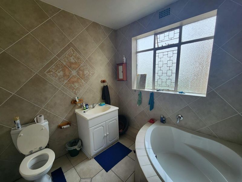 A functional bathroom featuring a built-in corner bathtub, vanity cabinet with basin, and tiled wall and floor finishes with security bars on the window.