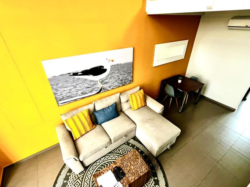 A bright living area featuring vibrant yellow walls, tiled flooring, and a wall-mounted air conditioning unit.