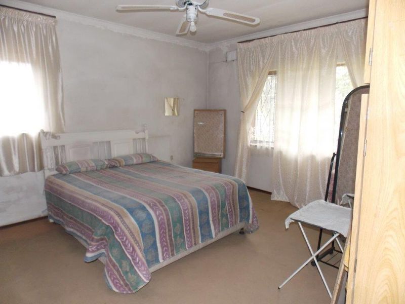 A bedroom featuring a ceiling fan and security bars on the windows, requiring cosmetic updates to the walls and flooring to improve its condition.