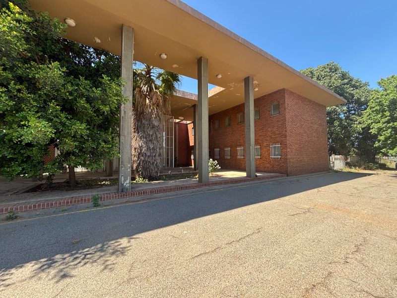 Front exterior view of a brick office building featuring a covered walkway supported by concrete pillars and security-barred windows.