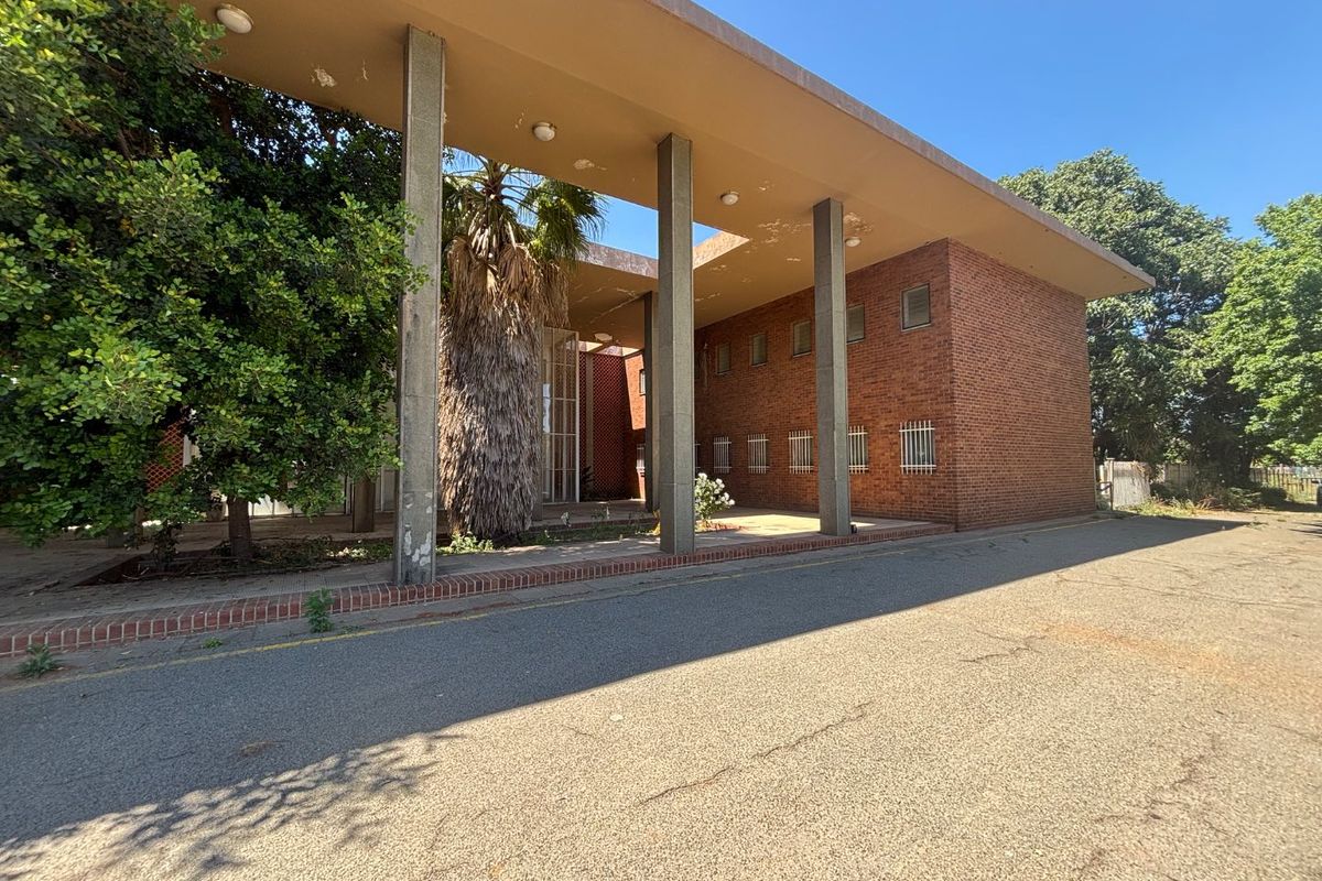 Front exterior view of a brick office building featuring a covered walkway supported by concrete pillars and security-barred windows.