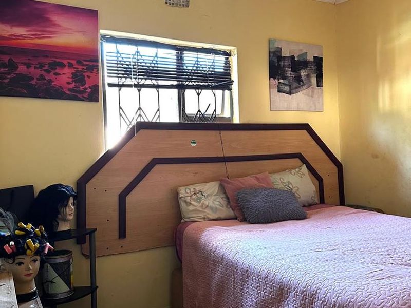 A bedroom featuring tiled flooring, a built-in headboard, and a window with security bars, requiring cosmetic updates to improve the overall aesthetic.
