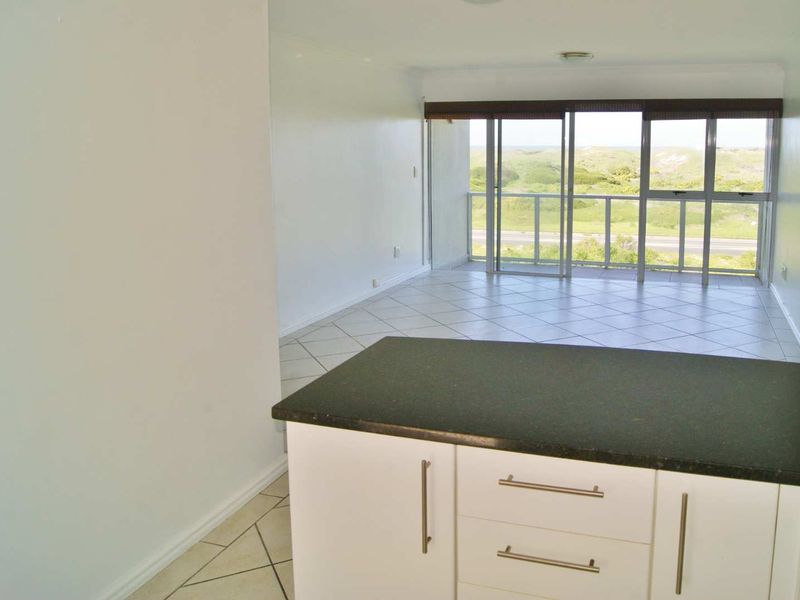 Open plan living area featuring a kitchen island with stone countertop, tiled flooring, and sliding glass doors leading to a balcony with scenic views.