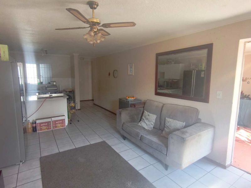 Open plan living area featuring tiled flooring, a ceiling fan, and a breakfast bar connecting to the kitchen space.
