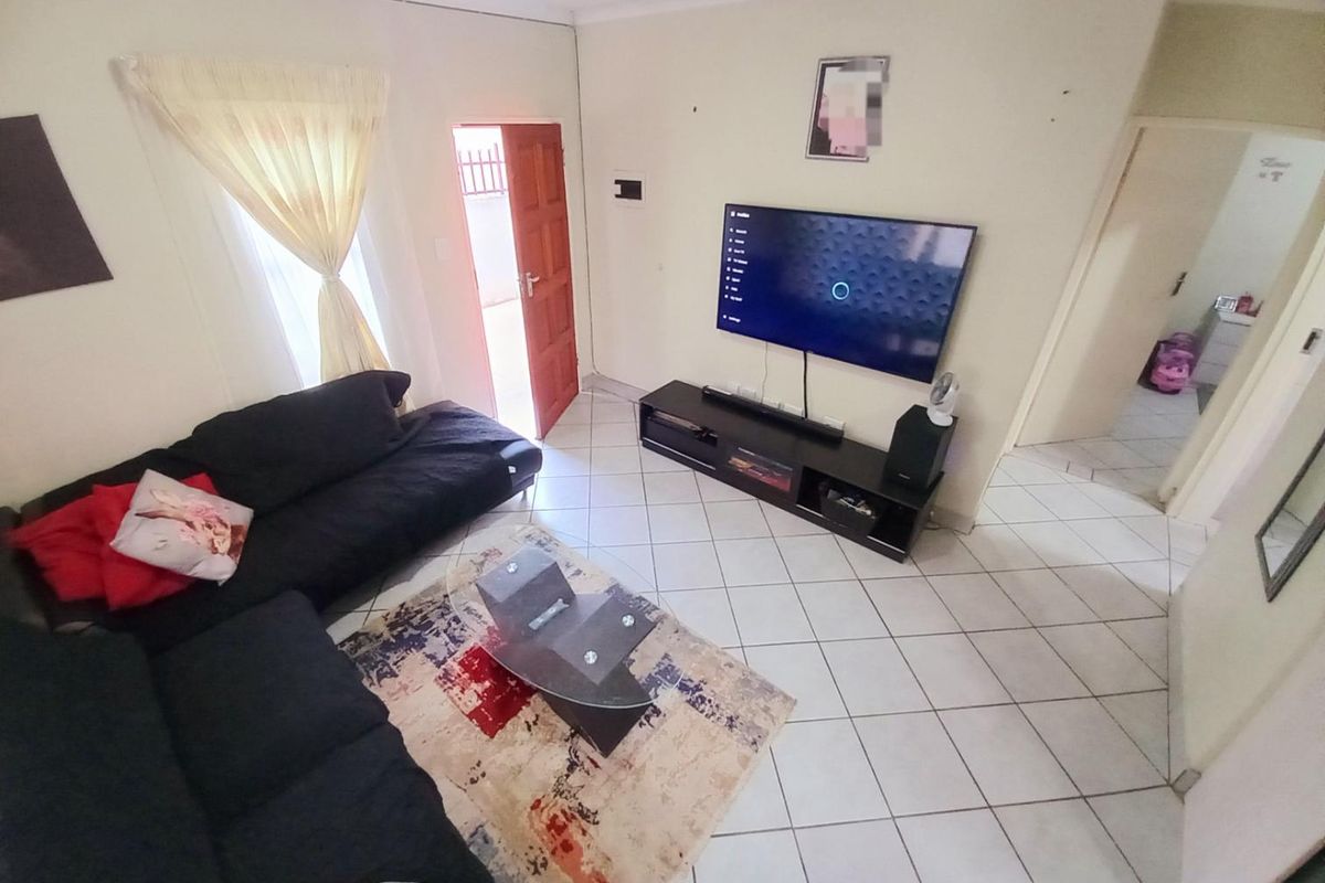 A functional living room featuring tiled flooring, a wall-mounted television, and direct access to an exterior doorway.