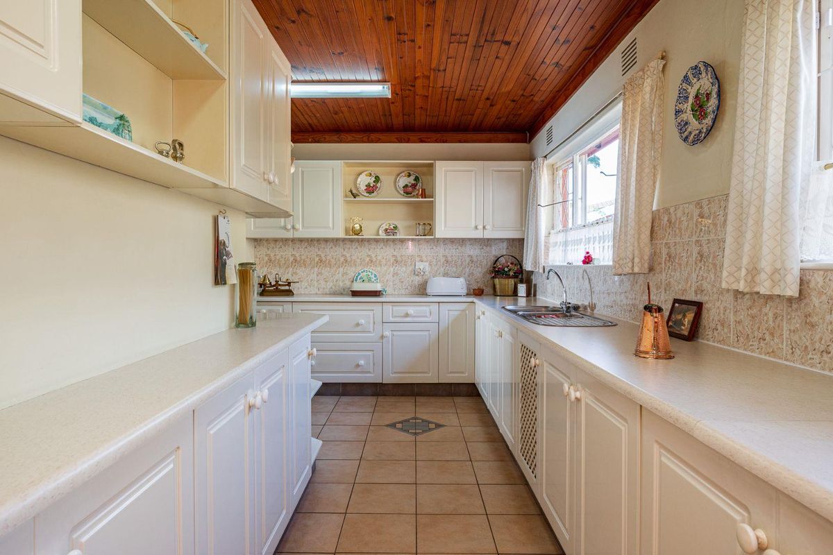 A functional kitchen featuring white cabinetry, laminate countertops, tiled backsplash, and a distinctive timber tongue and groove ceiling.