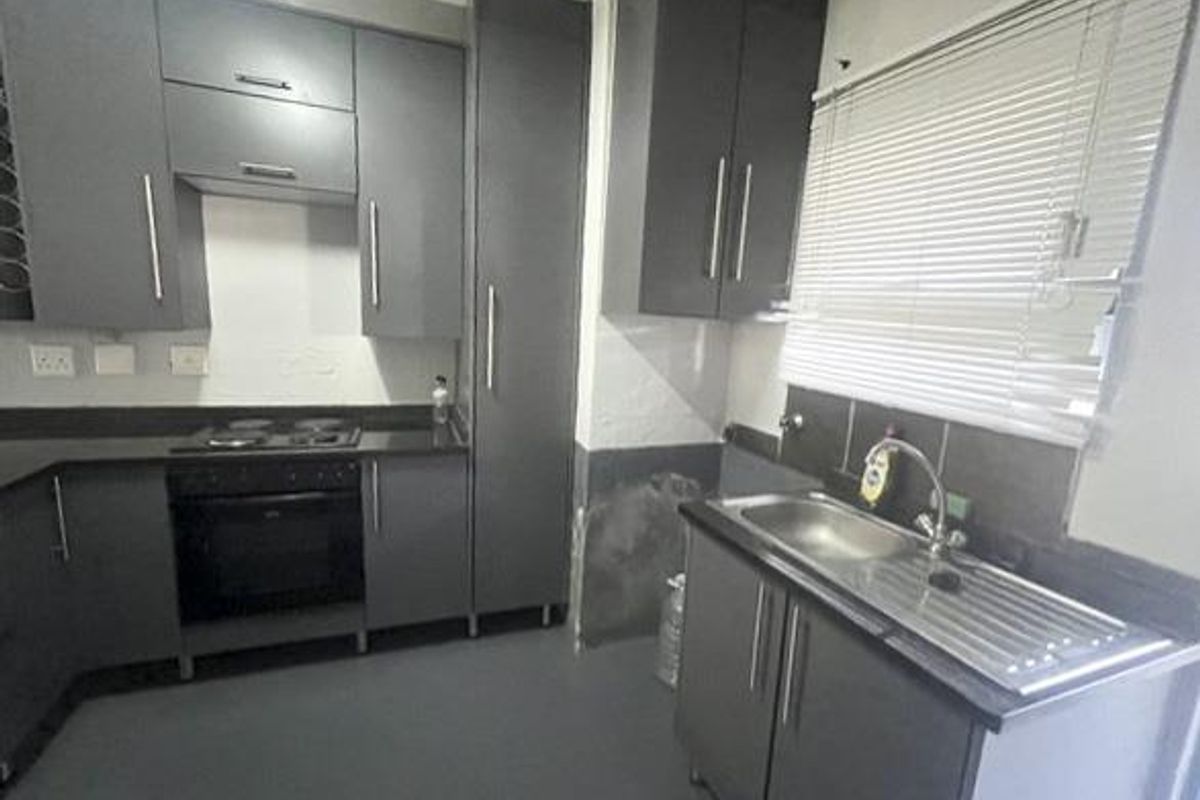 A functional kitchen featuring dark grey cabinetry, built-in oven and hob, and a stainless steel sink with a window view.